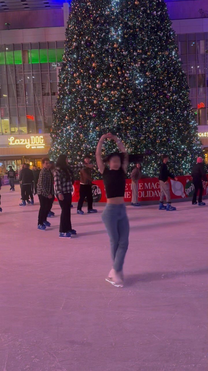 Fun Christmas Activities for Families: 18 Ideas With Photos 5 A woman ice skating on an outdoor rink in front of a large Christmas tree.