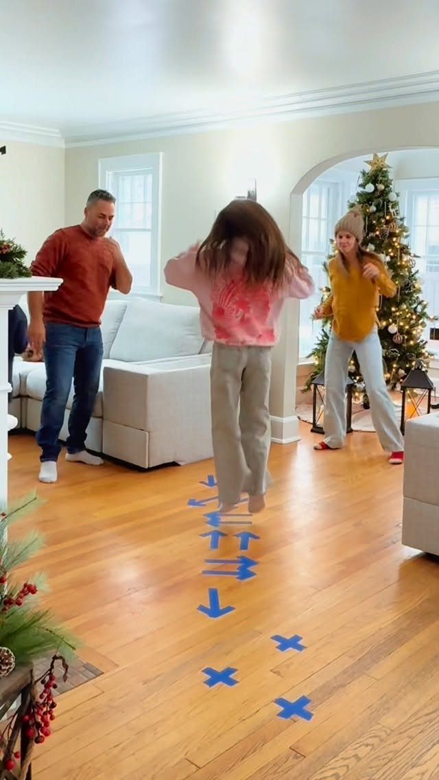 Fun Christmas Activities for Families: 18 Ideas With Photos 14 A young girl jumps over blue tape arrows on a wooden floor during a family game.
