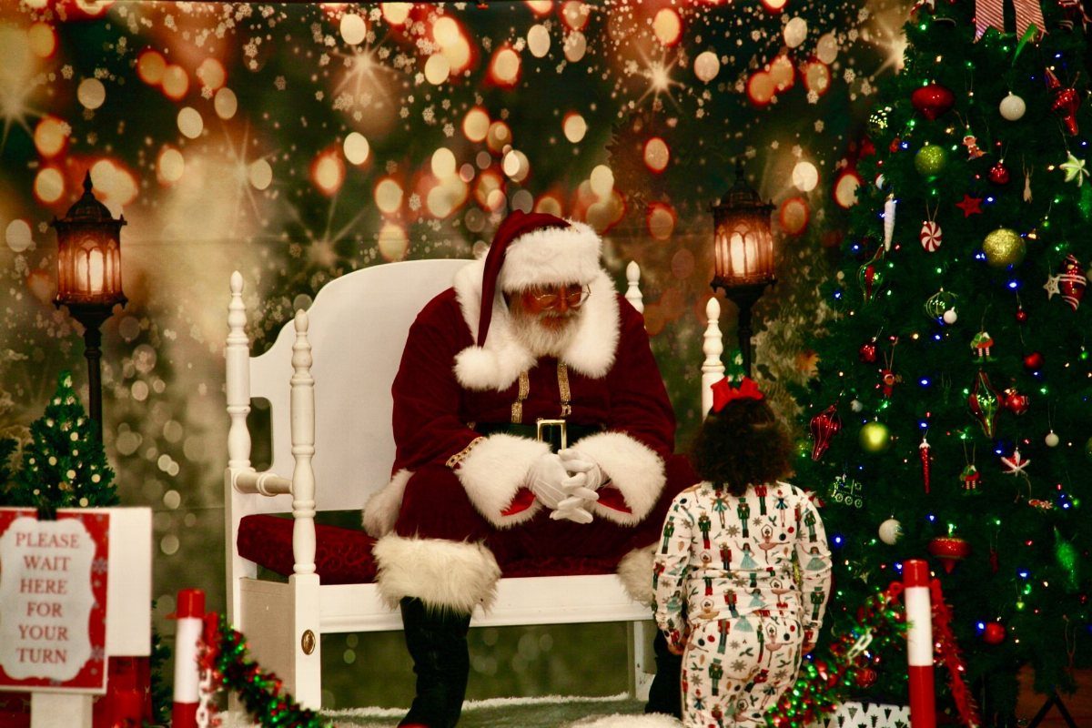 Fun Christmas Activities for Families: 18 Ideas With Photos 6 Santa Claus sitting in a white chair meeting a small child in festive pajamas.