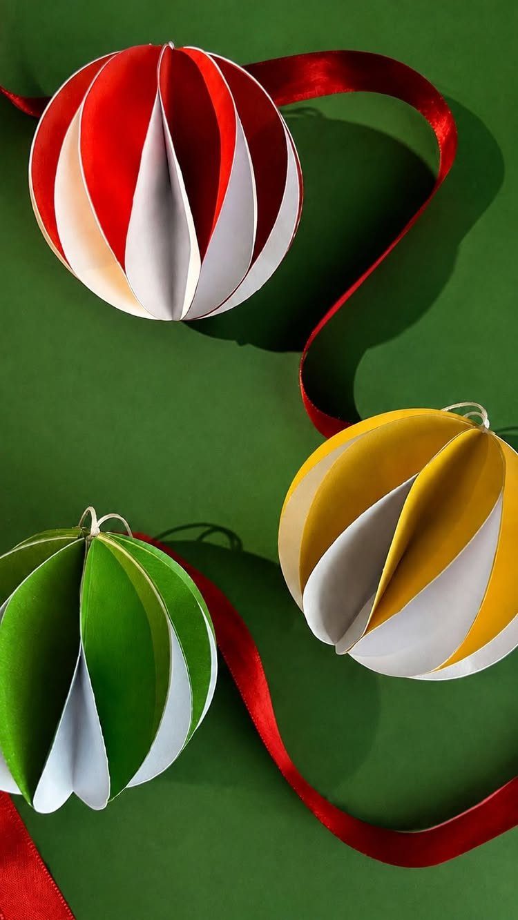 Three colorful spherical paper ornaments with red ribbons on a green background.