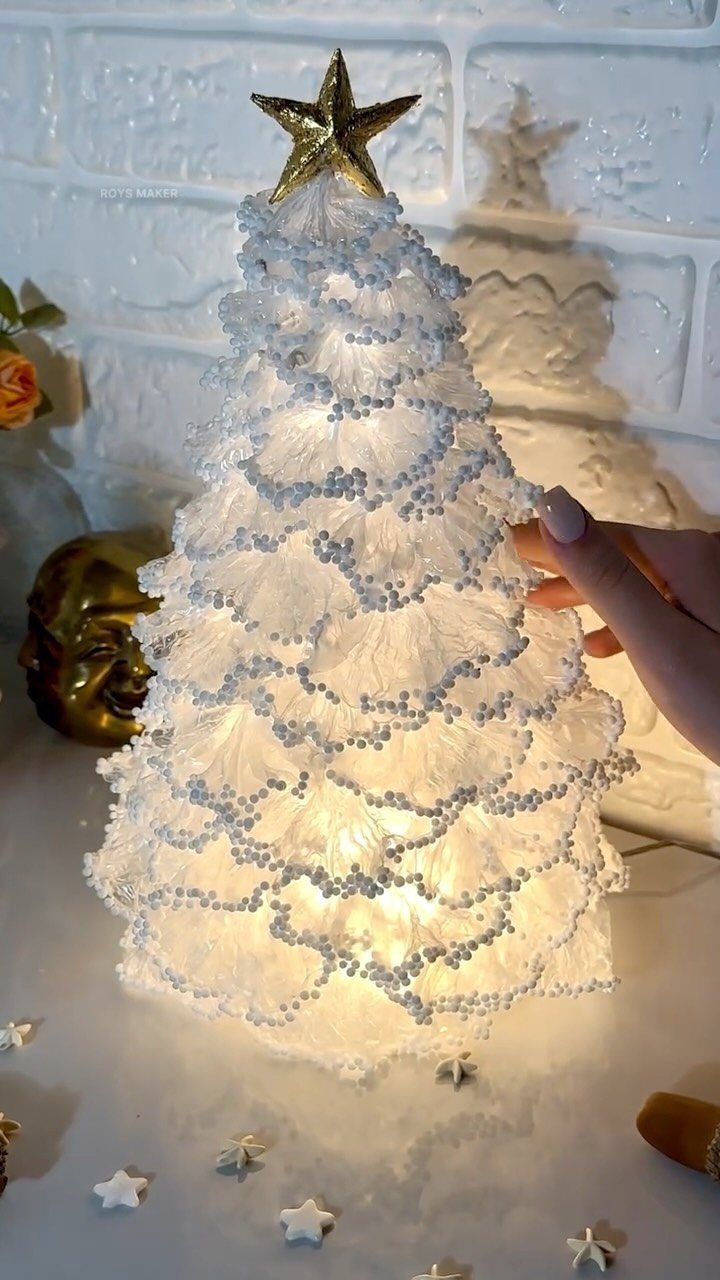 A glowing white textured Christmas tree with a gold star topper being touched by a hand.