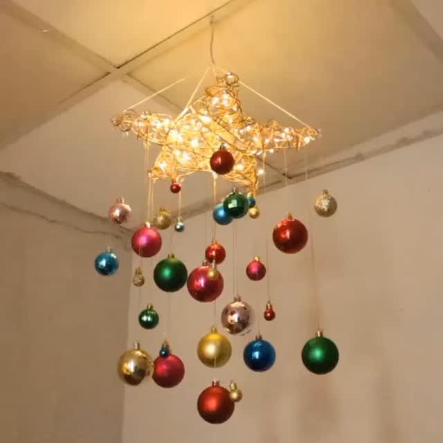 A glowing star ornament hanging from a ceiling with colorful Christmas baubles suspended below it.
