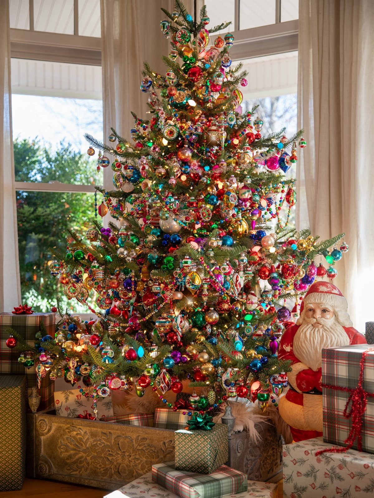 A decorated Christmas tree with colorful vintage ornaments and gifts at its base.
