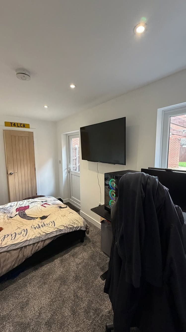 Garage into Bedroom: 4 Ideas From Guesthouse to Home Theater 2 A converted room featuring a bed, a wall-mounted television, and a computer desk setup.