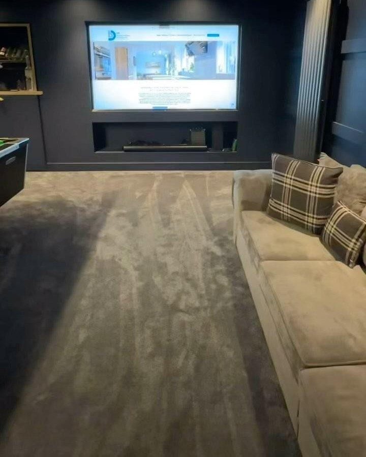 Garage into Bedroom: 4 Ideas From Guesthouse to Home Theater 4 Large television screen on a dark wall above a recessed shelf in a room with grey carpet and a beige sofa.
