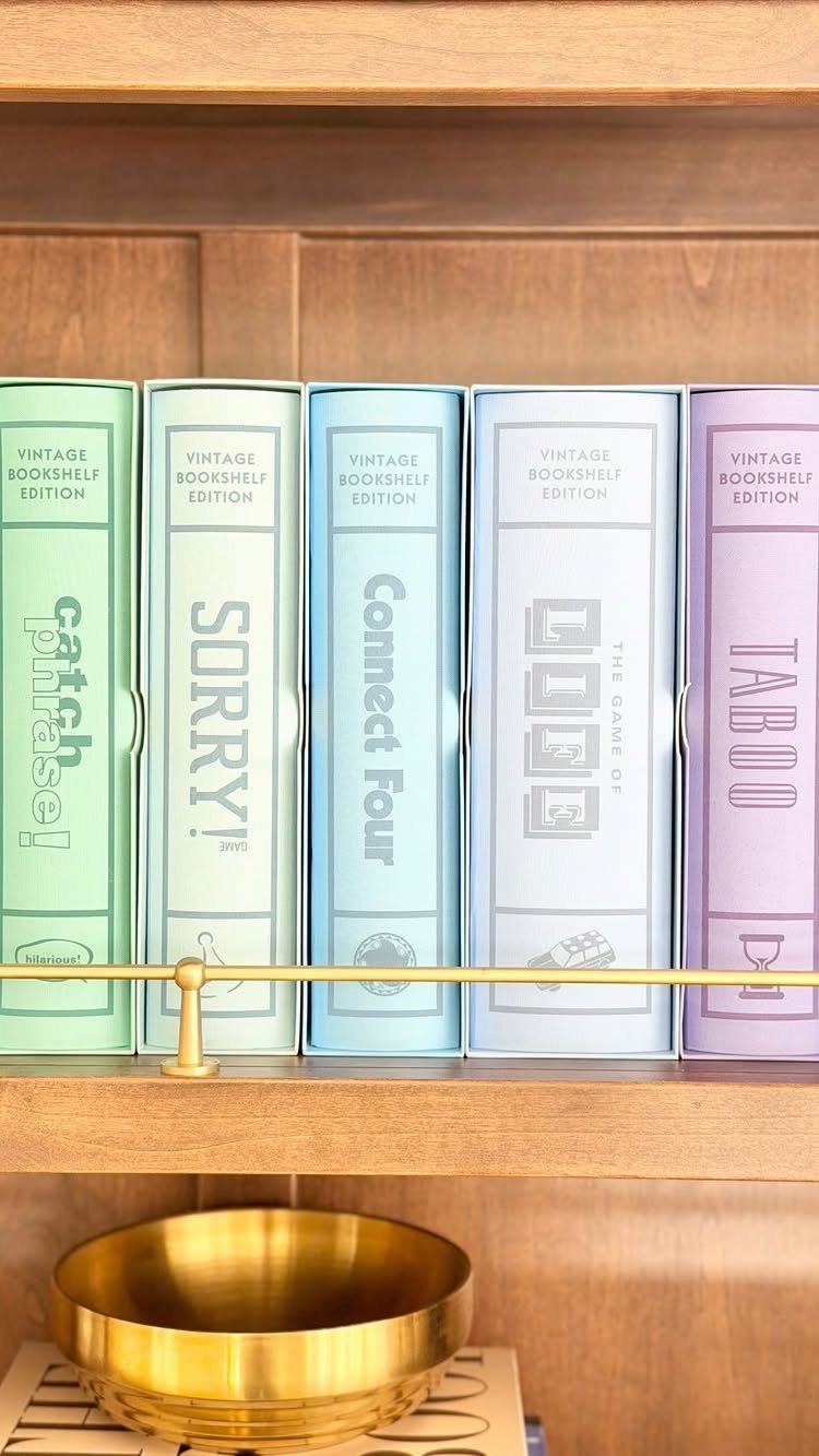 Vintage edition board game boxes in pastel colors lined up on a wooden shelf.
