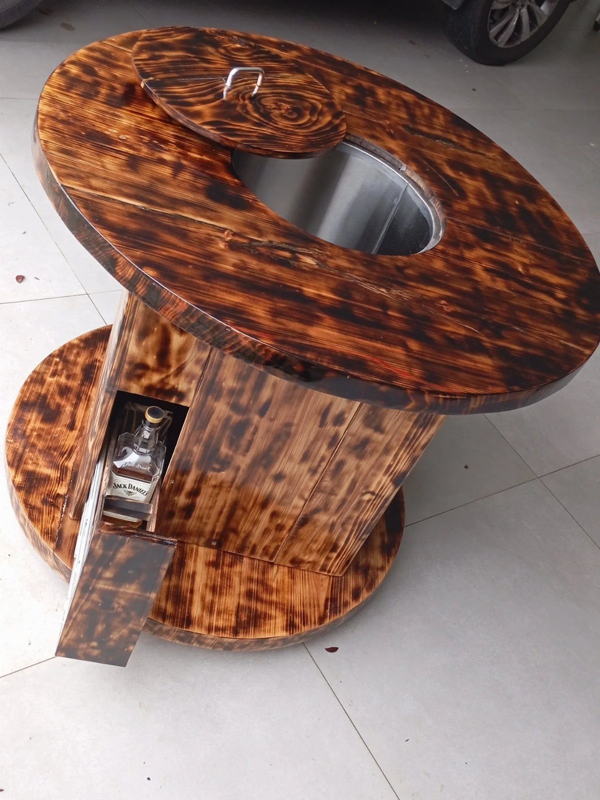 A dark stained wooden cable reel repurposed into a circular bar table with an ice bucket.