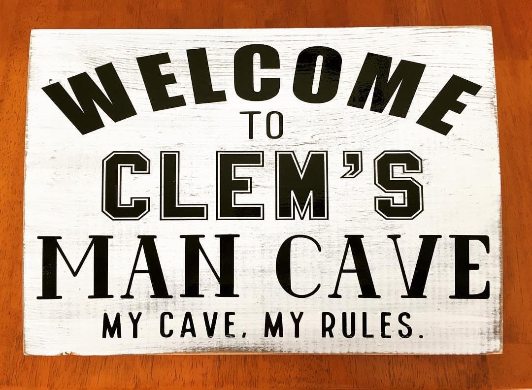 White wooden sign with black text welcoming visitors to Clem's Man Cave.