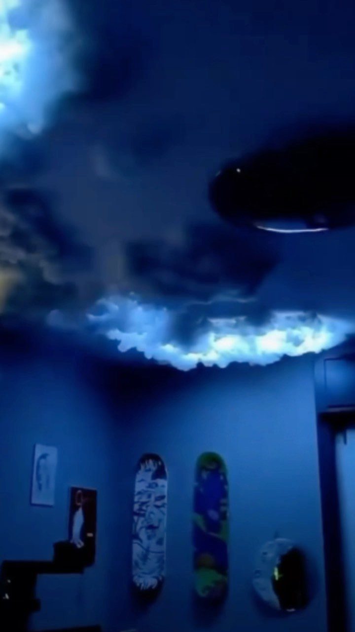 Blue glowing cloud structures on a ceiling above skateboards mounted on a wall.