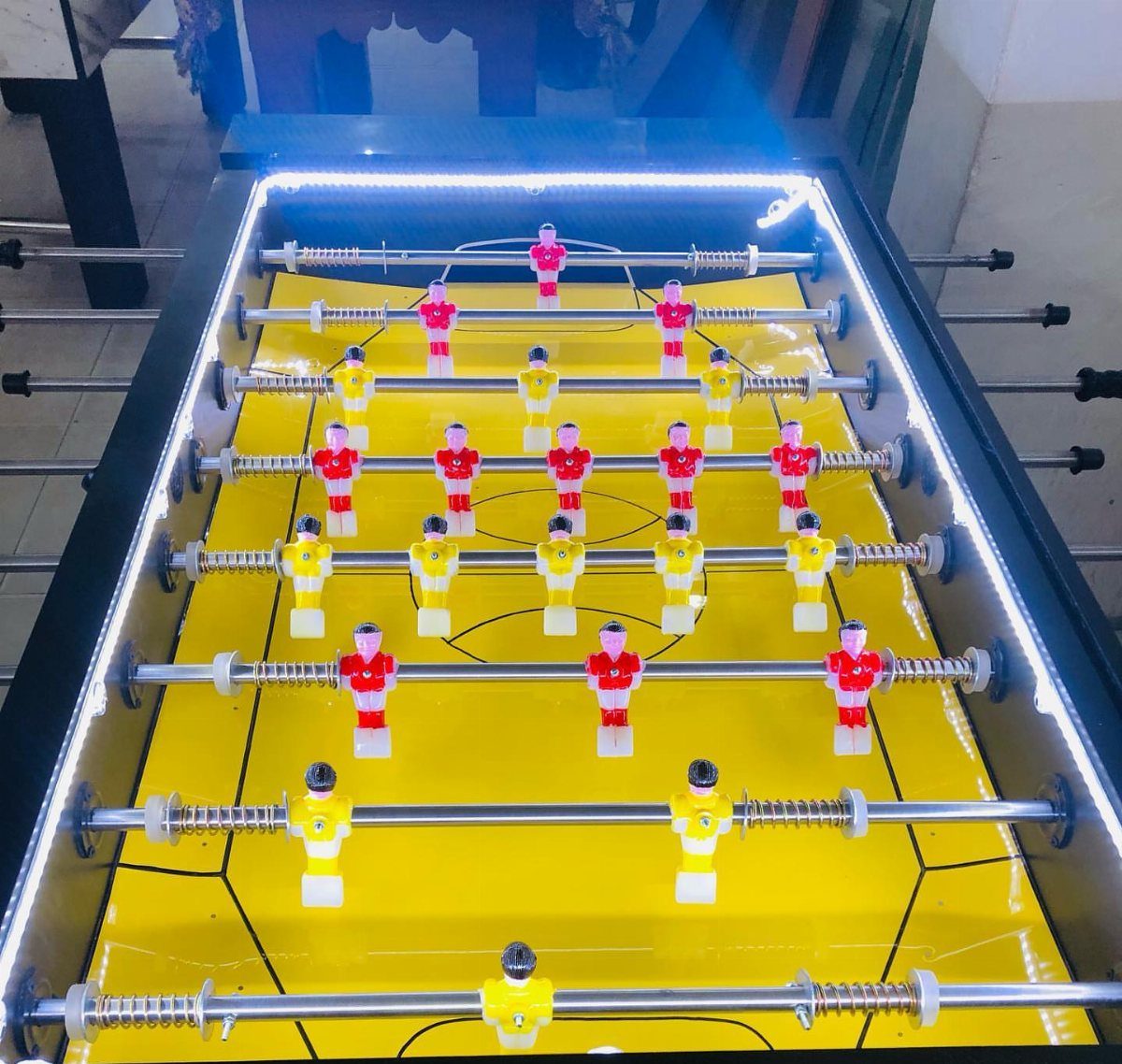Foosball table with yellow field, red and yellow players, and blue LED lighting.