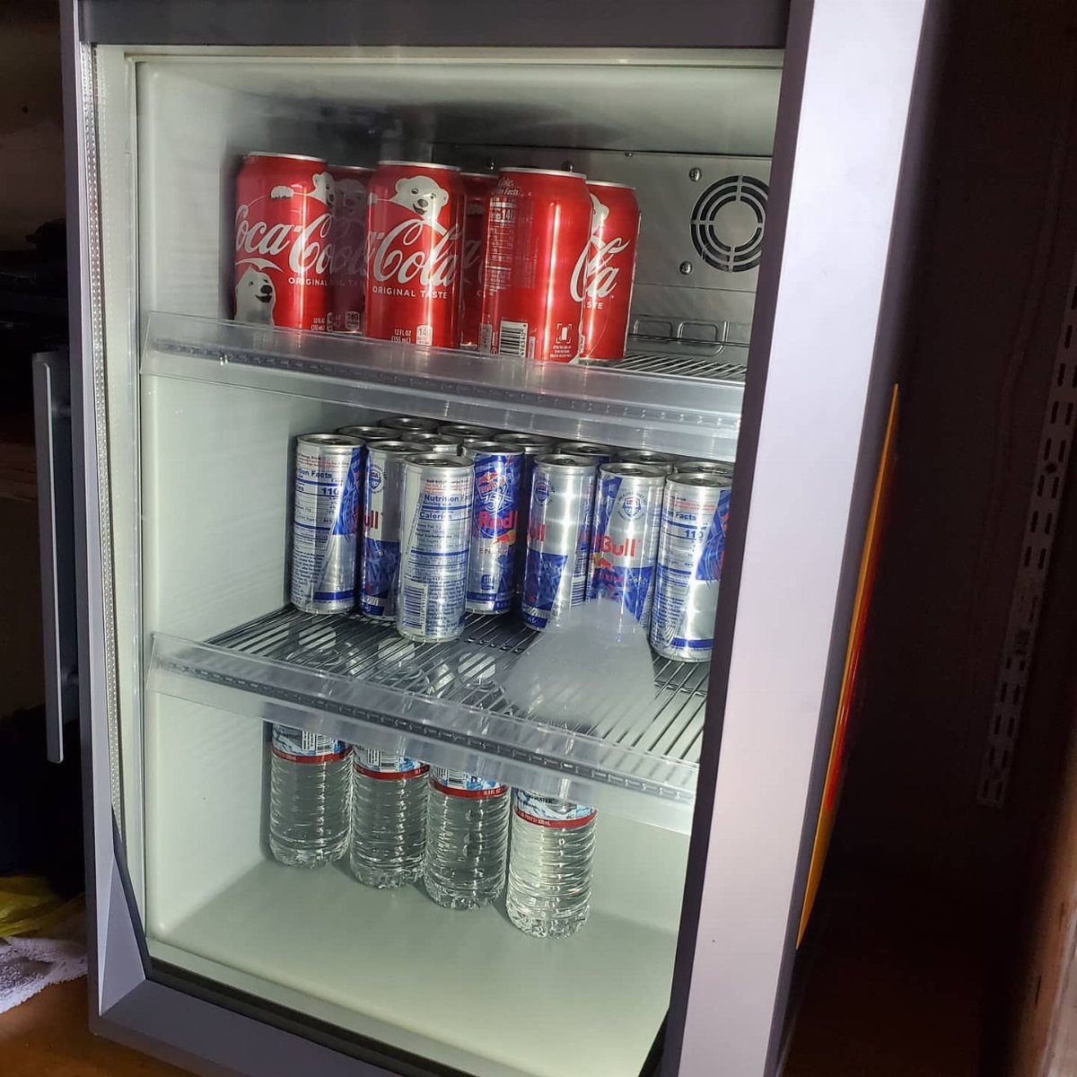 An open mini fridge stocked with various cans of soda and bottles of water.
