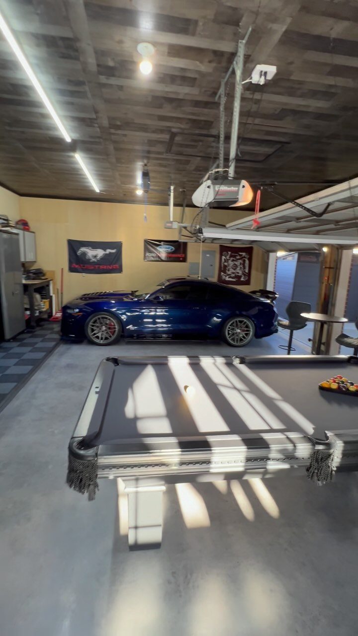 A blue sports car parked in a garage behind a black pool table.
