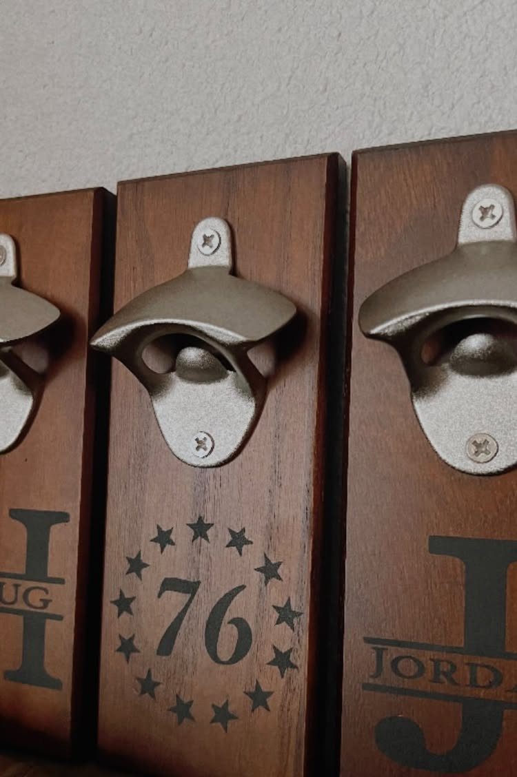 Three wooden wall-mounted bottle openers with metal openers and custom dark wood engravings.