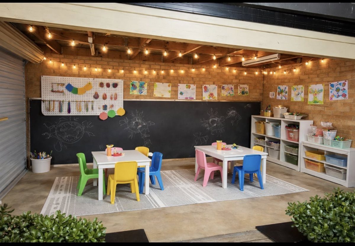 17 Garage Playroom Ideas for Safe, Creative Kid Space 4 Two white activity tables with colorful chairs sit on a rug in a brick-walled playroom.