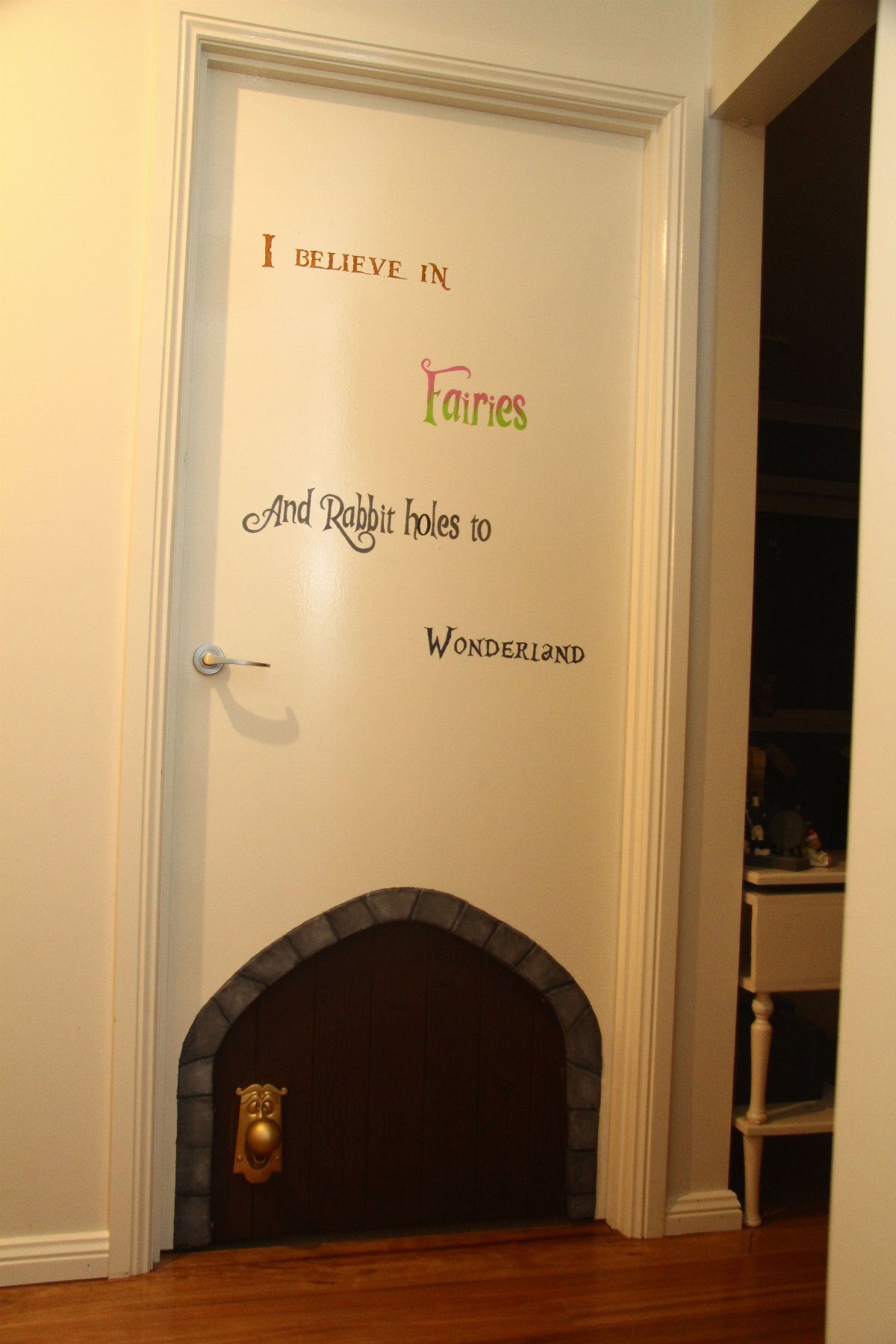 17 Garage Playroom Ideas for Safe, Creative Kid Space 10 White door with whimsical painted text and a small dark arched rabbit hole at the bottom.