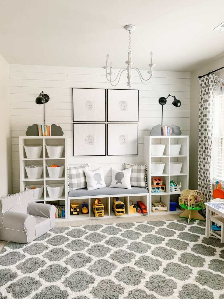 17 Garage Playroom Ideas for Safe, Creative Kid Space 8 A grey cushioned bench with white pillows sits above toy storage cubbies in a bright playroom.