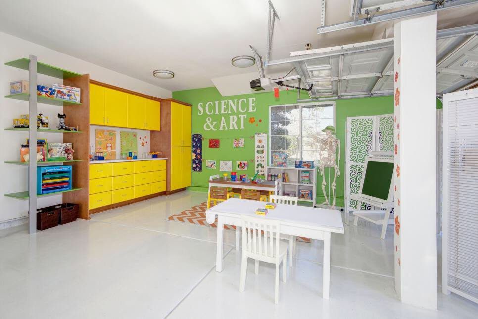17 Garage Playroom Ideas for Safe, Creative Kid Space 11 A bright playroom with yellow cabinets, a white activity table, and green walls on a white floor.
