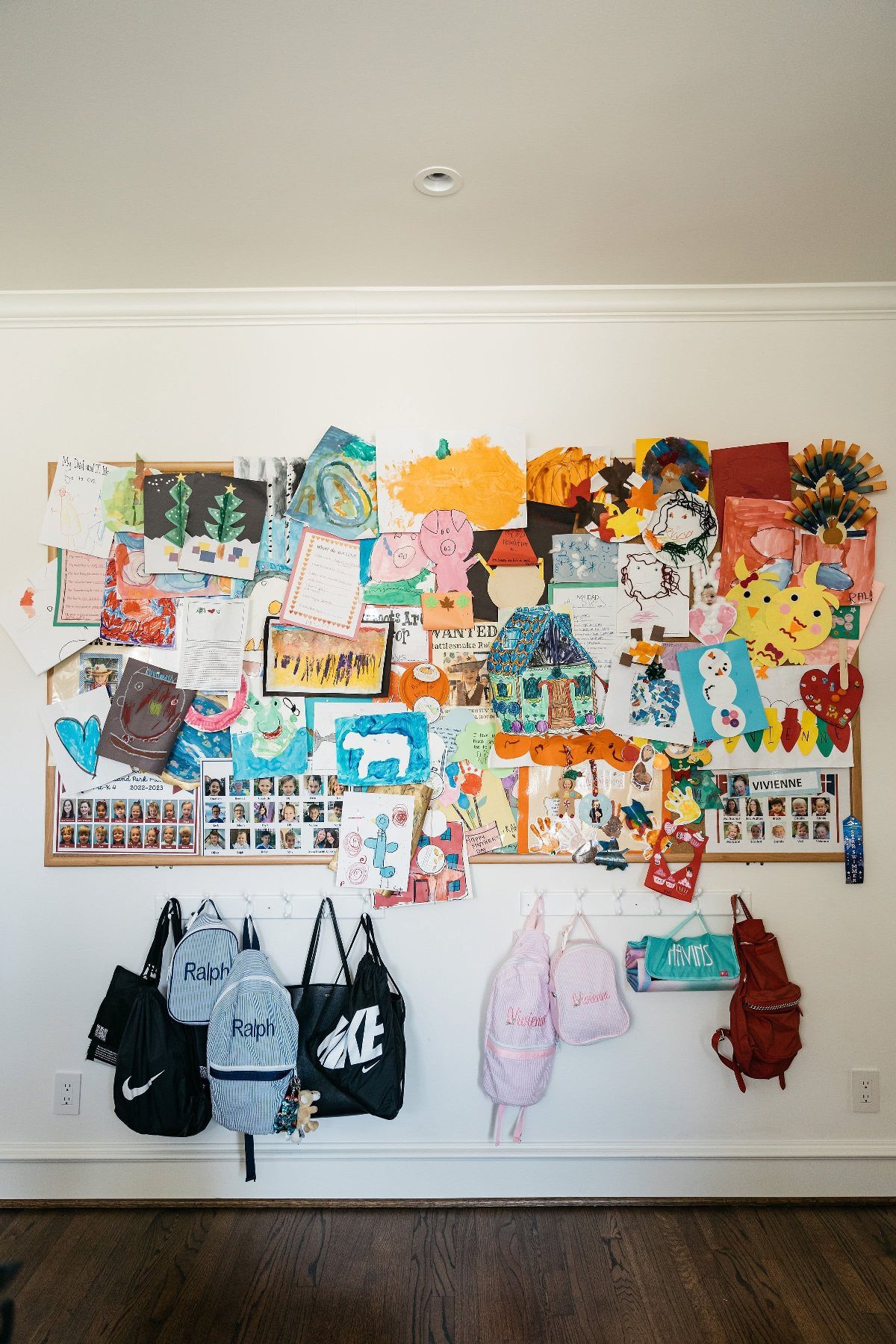 17 Garage Playroom Ideas for Safe, Creative Kid Space 7 Colorful children's artwork and drawings displayed on a large white wall above hanging backpacks.
