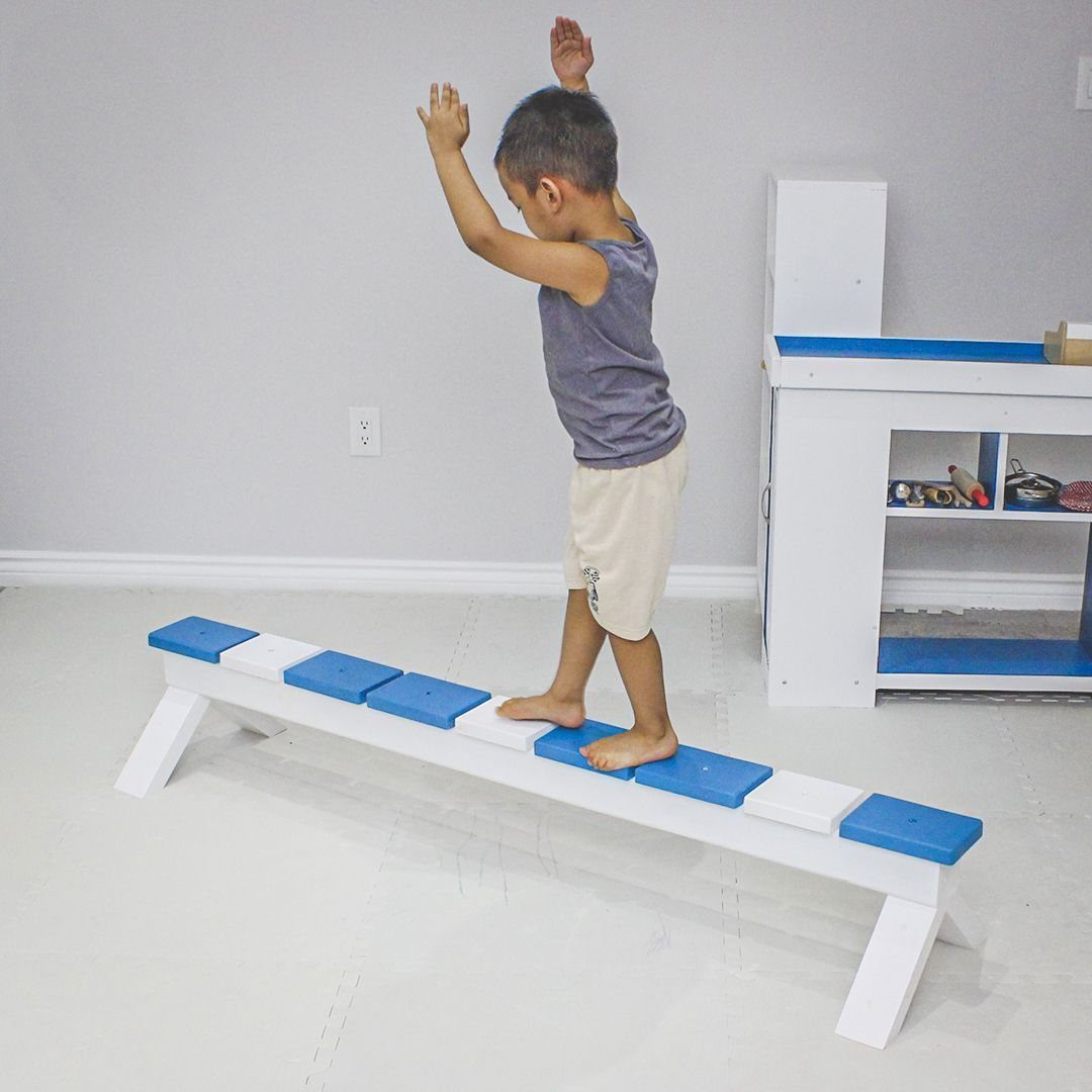 17 Garage Playroom Ideas for Safe, Creative Kid Space 15 A young boy balancing with raised arms on a low white and blue wooden beam.