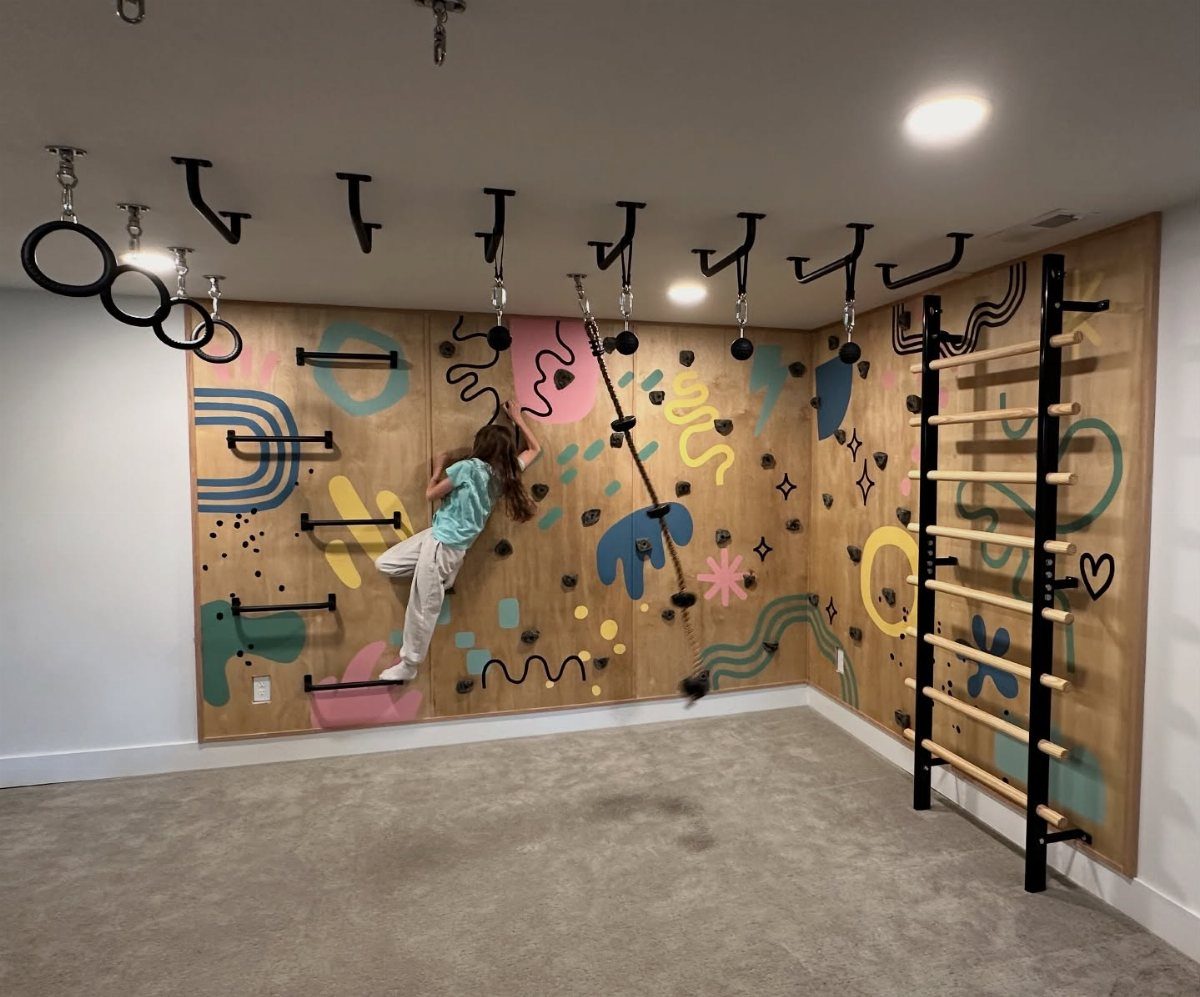 17 Garage Playroom Ideas for Safe, Creative Kid Space 2 A child climbing on a colorful wooden wall-mounted climbing structure in a playroom.