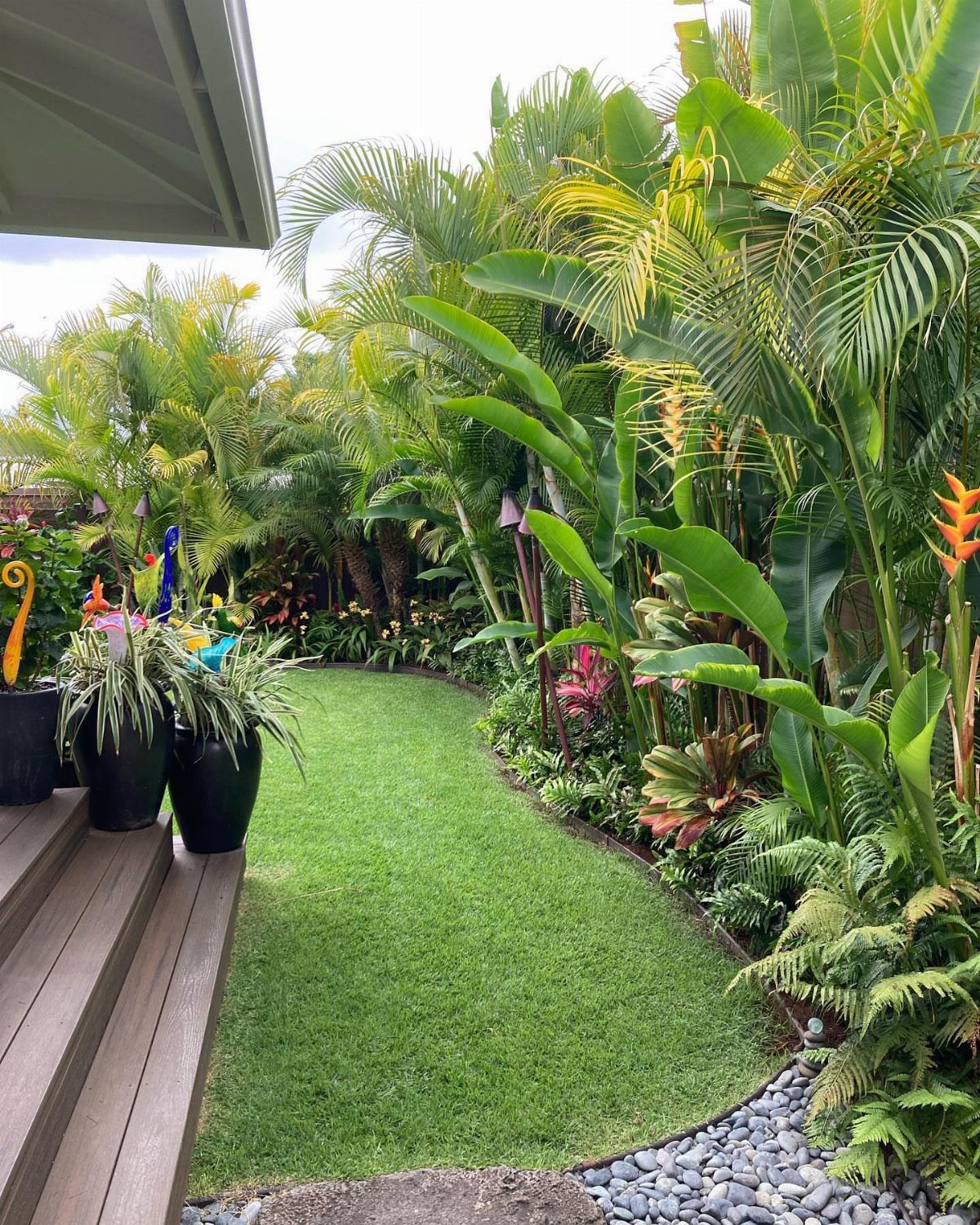 Lush tropical garden with large green palm leaves, ferns, and a curved green lawn.
