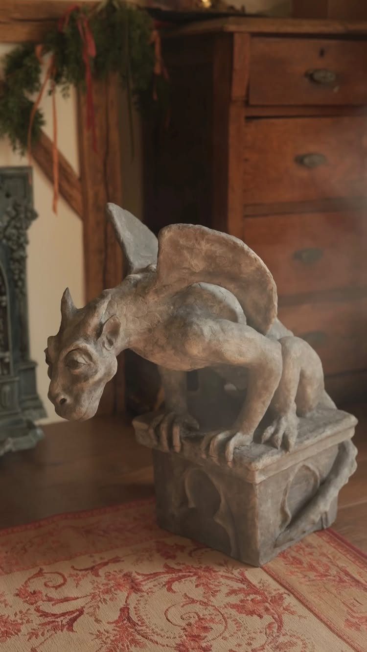 A grey stone gargoyle statue perched on a pedestal in a dimly lit room.