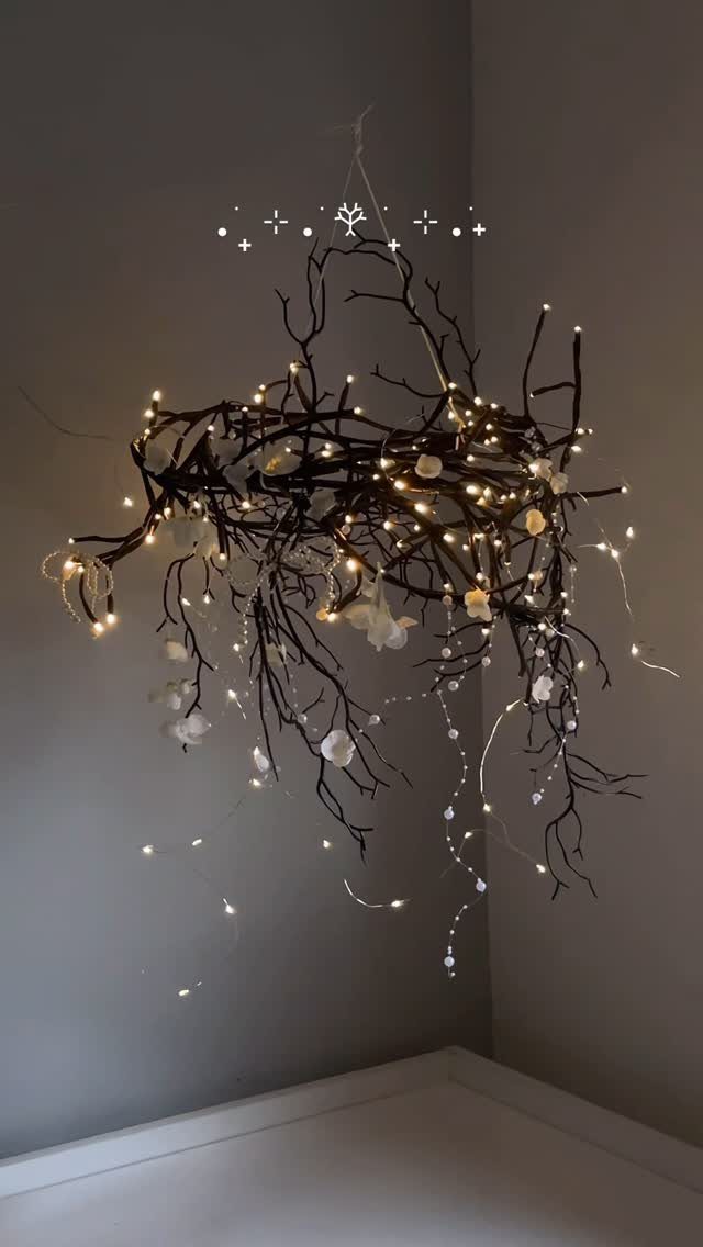 Dark branches decorated with warm fairy lights and white flowers hanging against a grey wall.