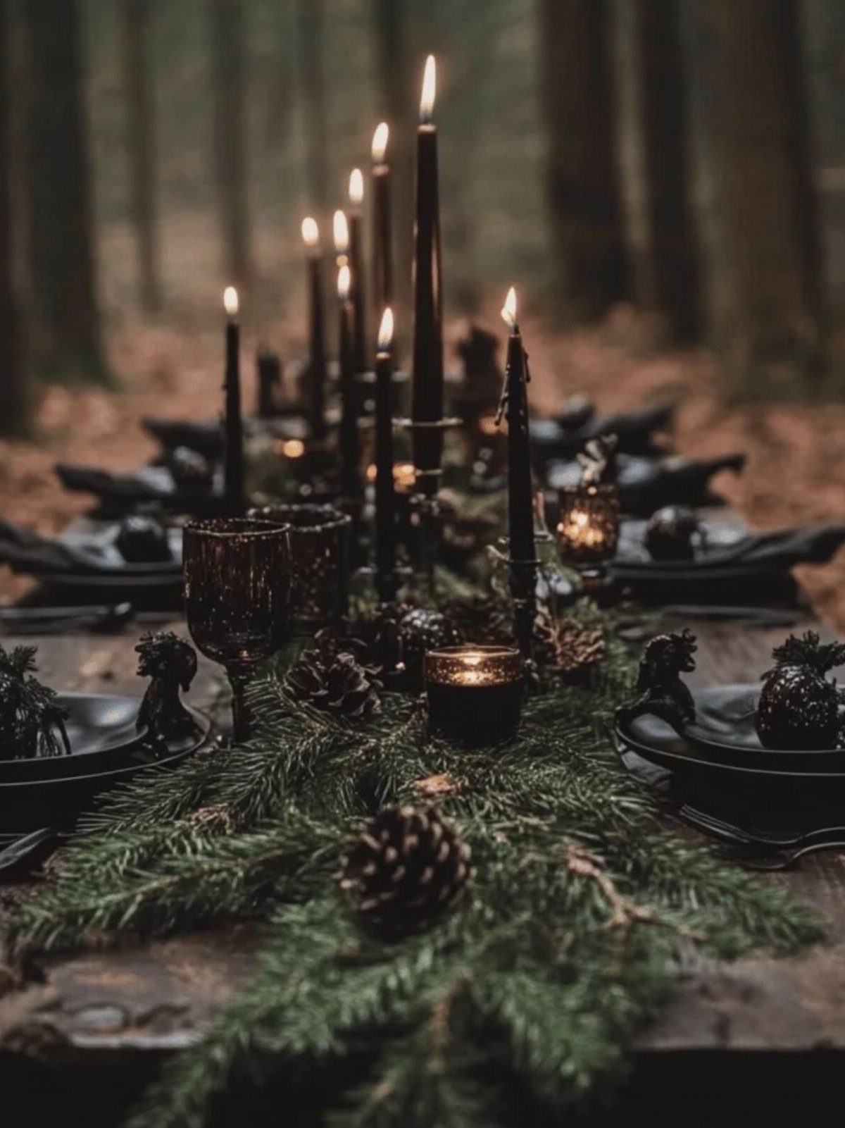 A gothic dining table set with black candles, pine branches, and dark plates in a forest.
