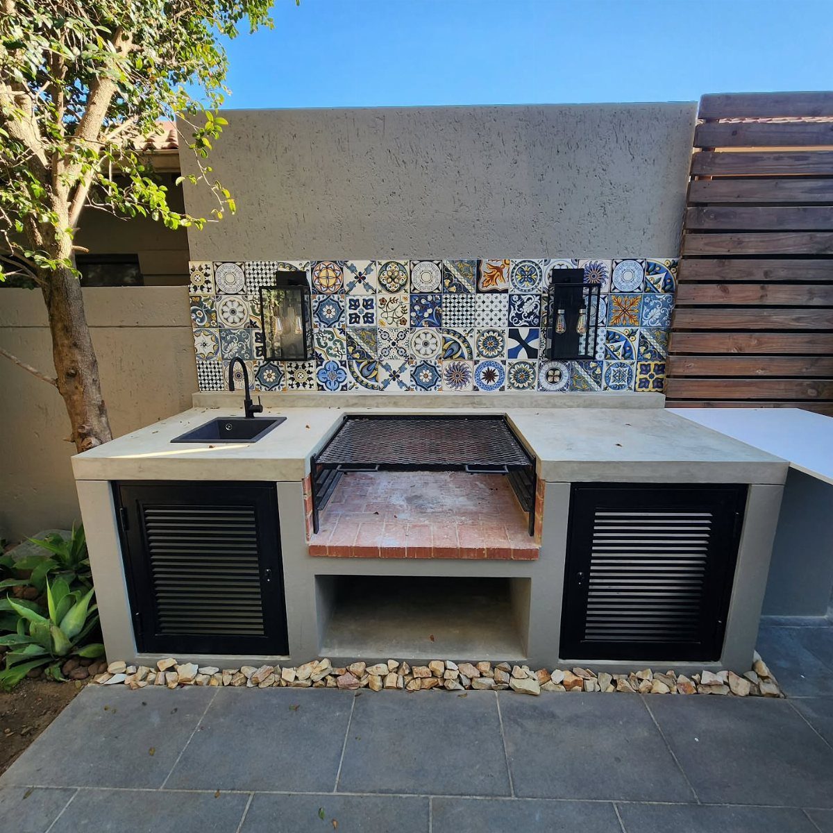 14 Outdoor Built In Grill Ideas for Every Backyard Style 13 Concrete outdoor grill station with a colorful patterned tile backsplash and a small black sink.