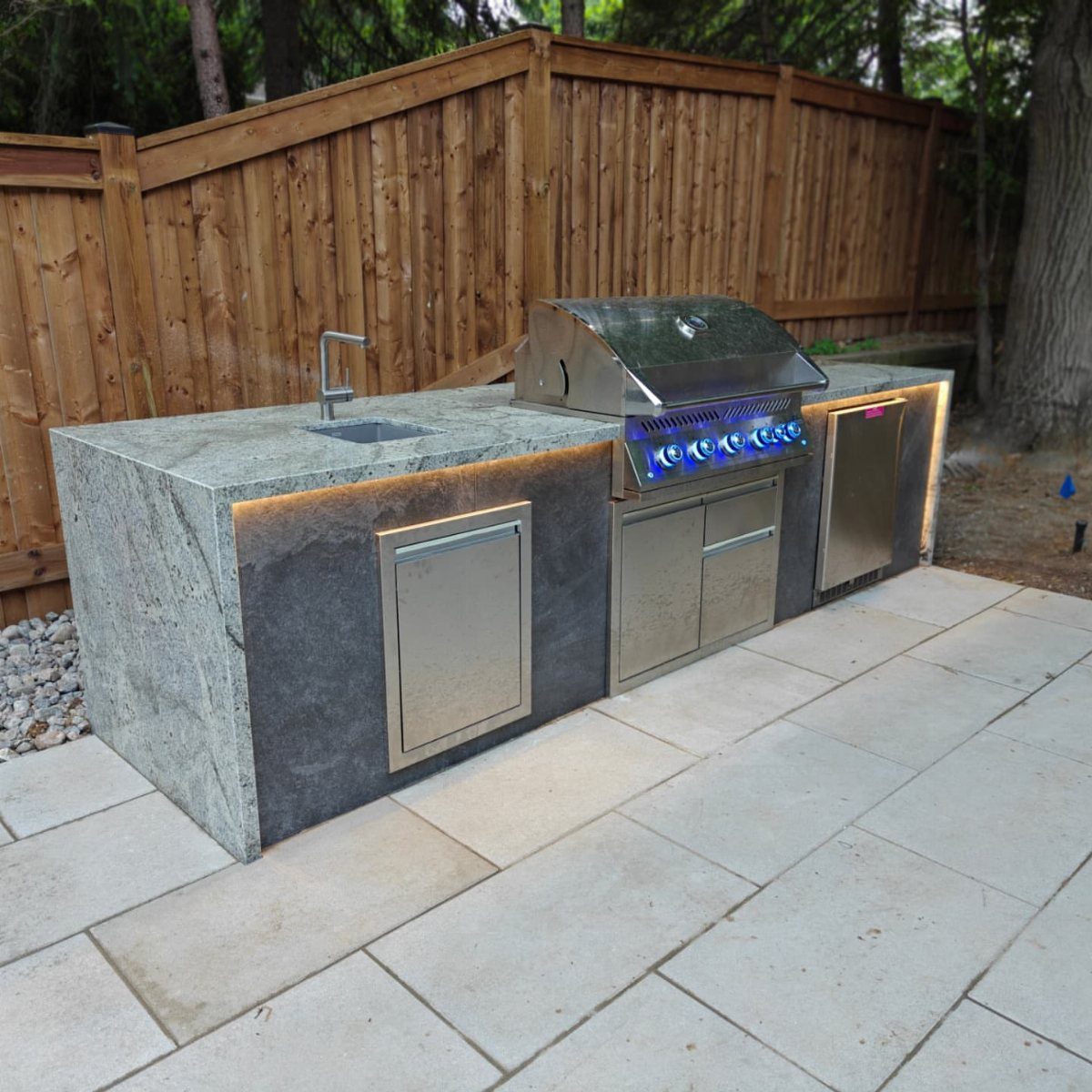 14 Outdoor Built In Grill Ideas for Every Backyard Style 12 Modern outdoor grill station with granite countertops and integrated LED lighting on a stone patio.