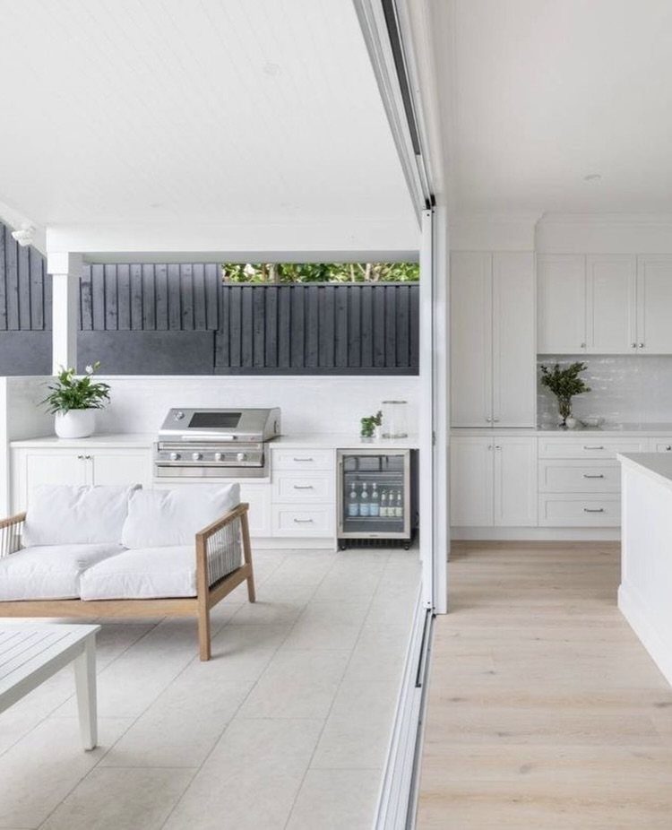 14 Outdoor Built In Grill Ideas for Every Backyard Style 10 A minimalist outdoor kitchen with white cabinets, a stainless steel grill, and a lounge chair.