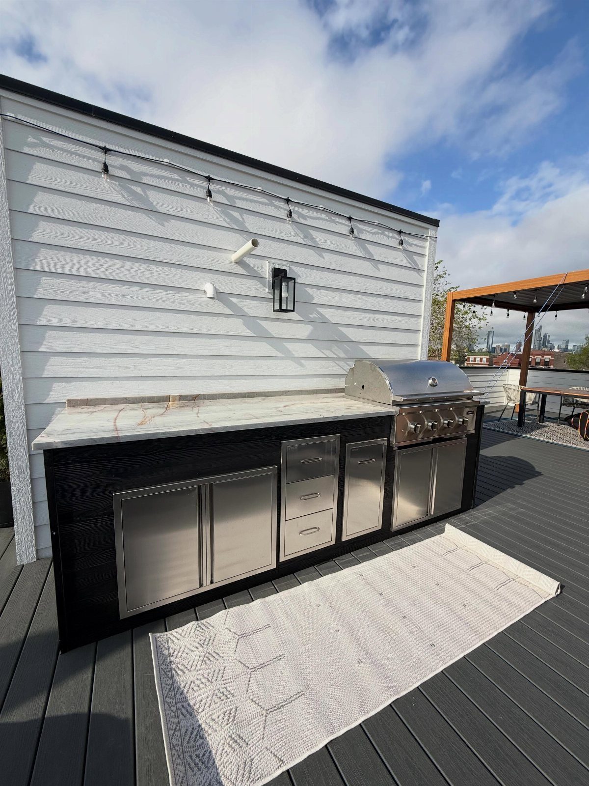 14 Outdoor Built In Grill Ideas for Every Backyard Style 7 Stainless steel grill and storage drawers with a white quartz countertop on a dark deck.