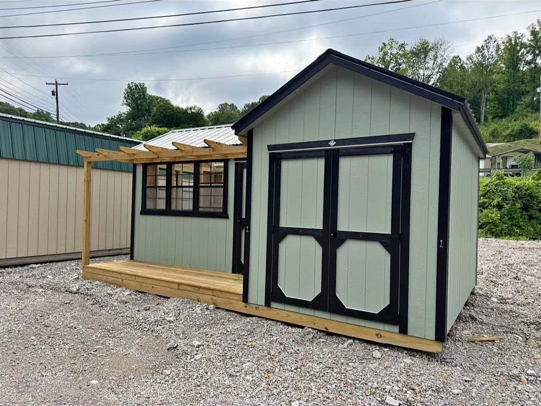 6 Painted Shed Colors for a Backyard That Actually Looks Planned 5 A sage green wooden shed with black trim and a small wooden pergola attached.