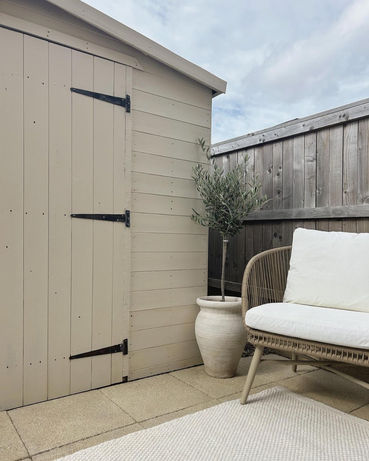 6 Painted Shed Colors for a Backyard That Actually Looks Planned 6 A light beige wooden garden shed with black hinges next to a patio chair.