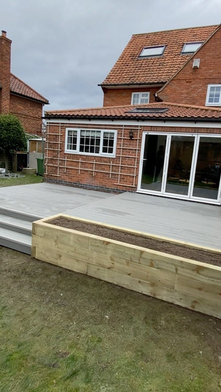 Raised Deck Frame: 8 Ideas From Wood Joists to Galvanized Steel 3 Grey wooden deck with built-in steps next to a brick house and a wooden garden bed.