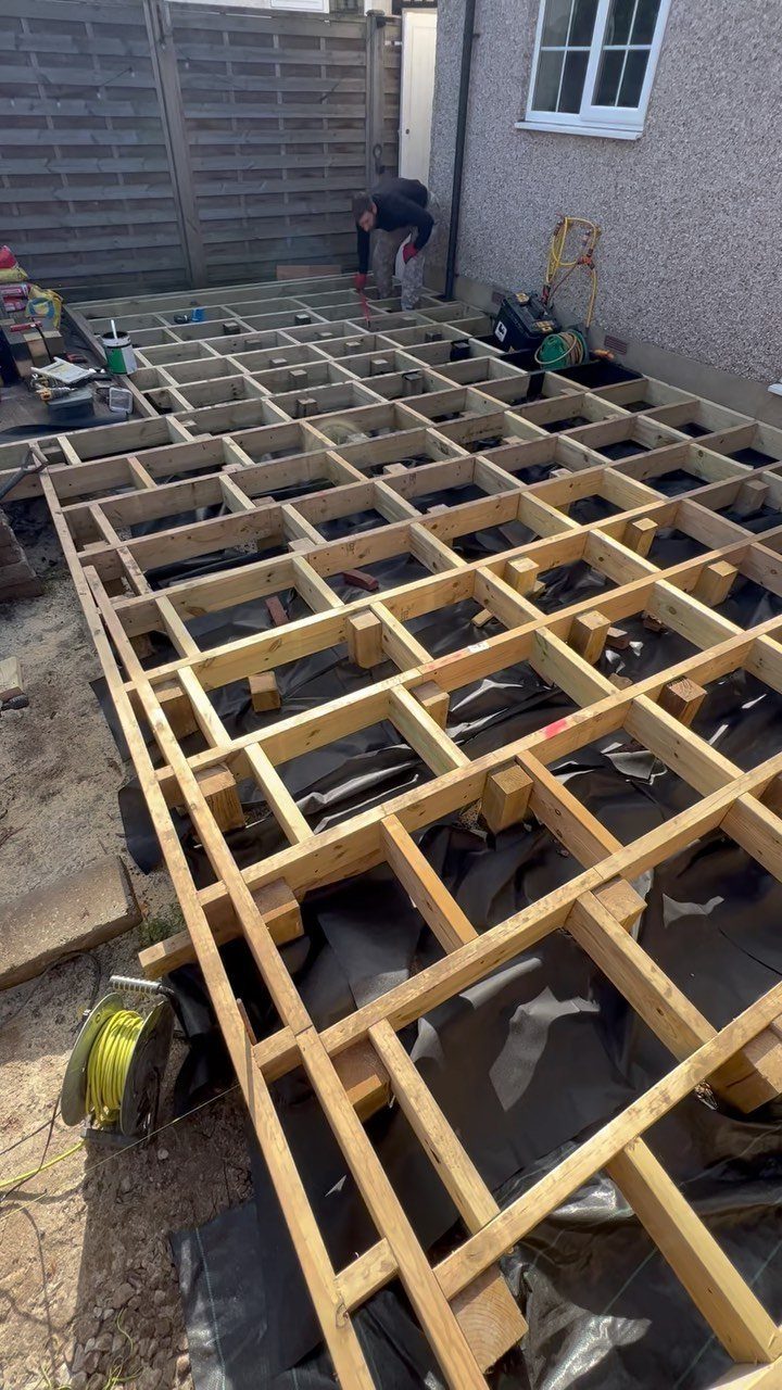 Raised Deck Frame: 8 Ideas From Wood Joists to Galvanized Steel 6 A wooden grid structure of a raised deck frame under construction on a black tarp.