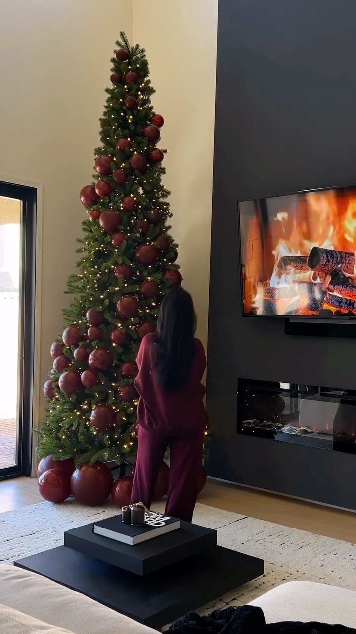 A tall green Christmas tree decorated with many large red ornaments and warm lights.
