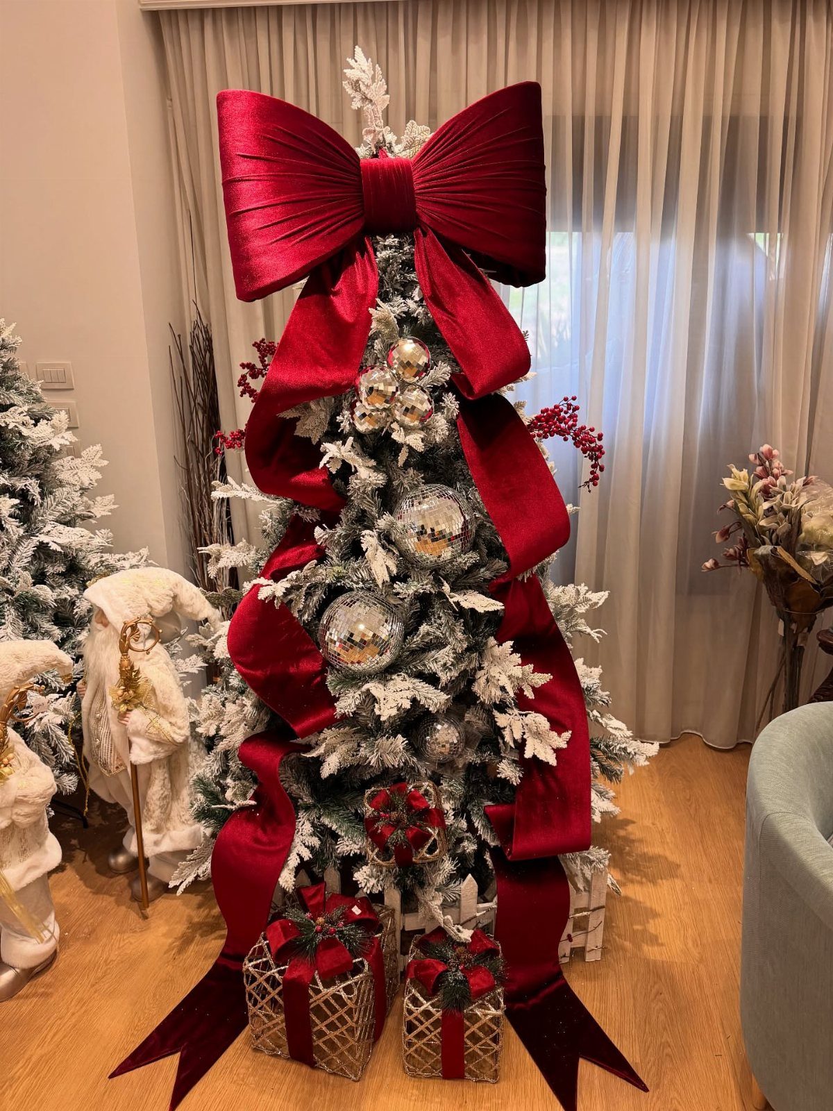 A flocked Christmas tree featuring a large red velvet bow topper and cascading red ribbons.