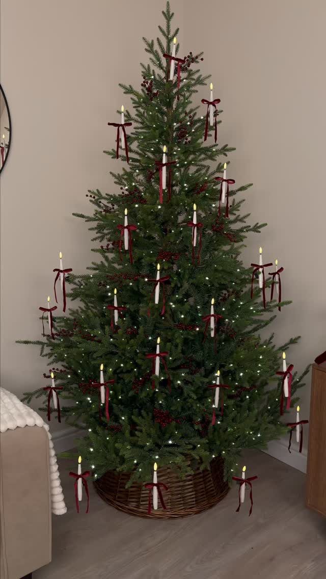 A green Christmas tree decorated with white candle ornaments and red ribbons in a wicker basket.