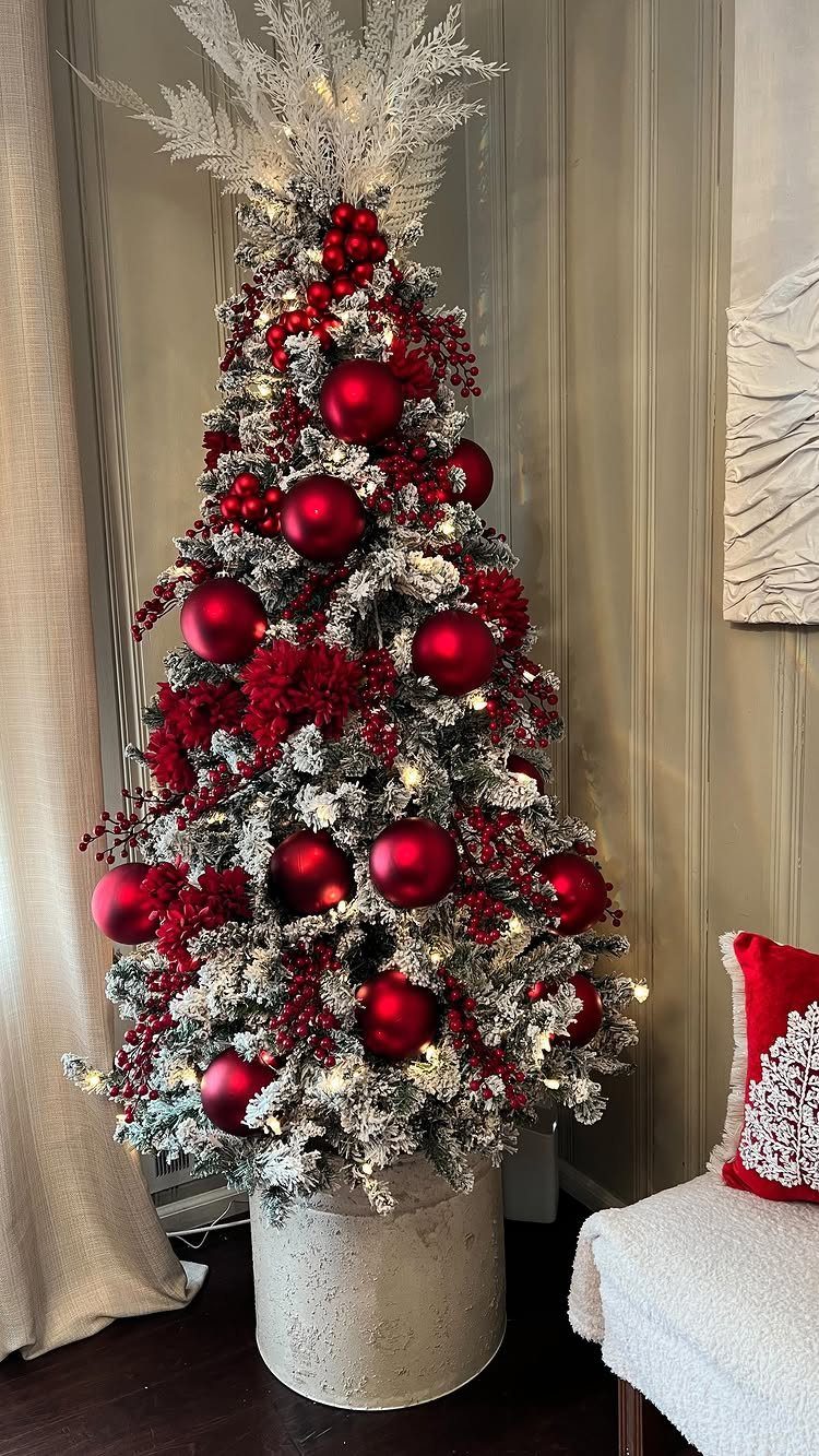Flocked Christmas tree decorated with red ornaments, red berries, and red flowers in a stone pot.