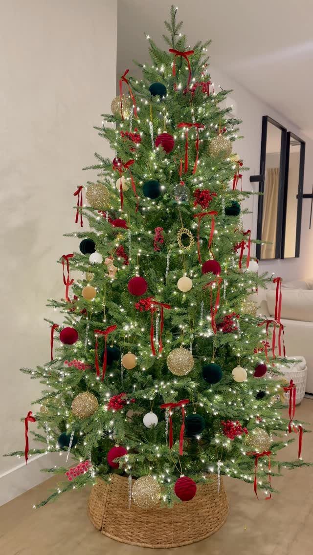 Decorated green Christmas tree with red ribbons and warm white lights in a wicker basket.