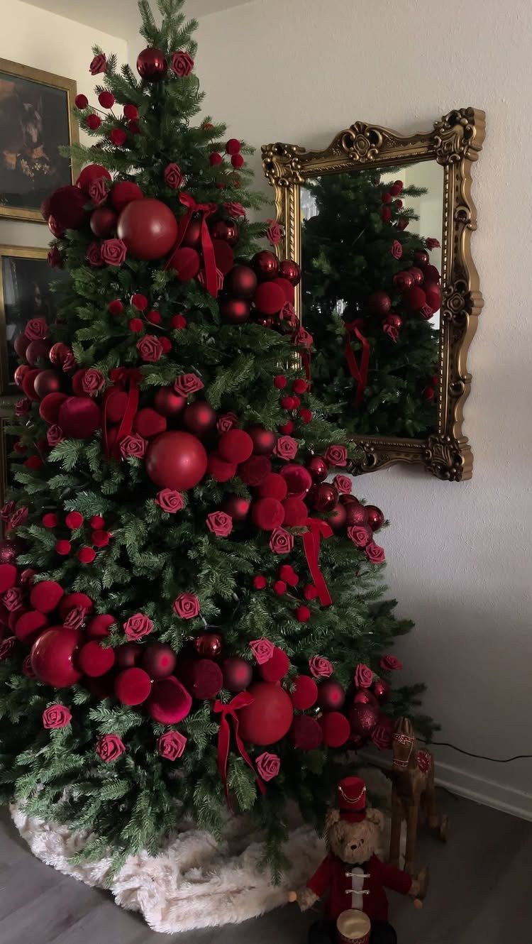 A decorated green Christmas tree with red ornaments, red roses, and red ribbons indoors.