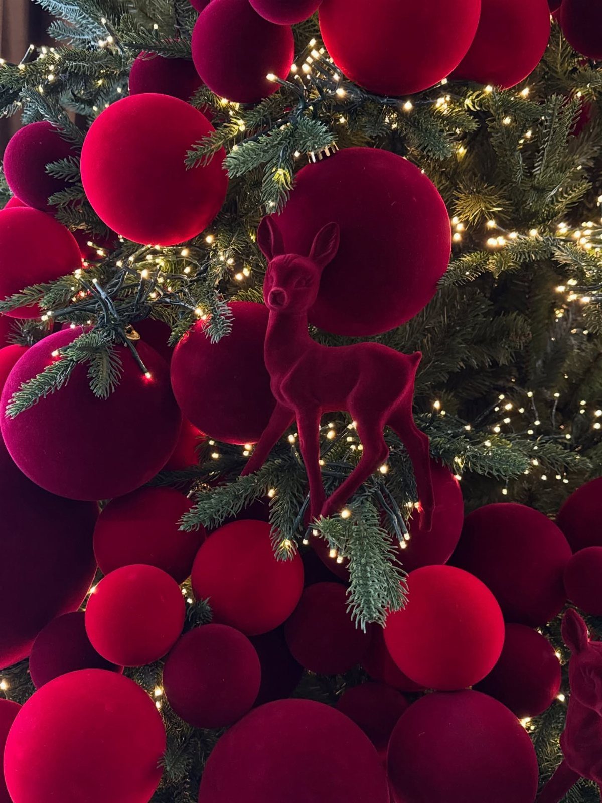 Red velvet Christmas ornaments and a reindeer decoration on a tree with warm lights.