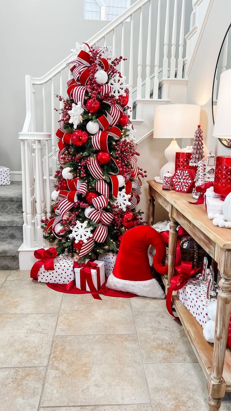 Decorated Christmas tree with red and white ornaments and ribbons standing next to a white staircase.